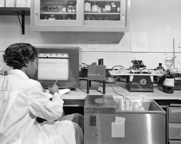 Black-and-white photo of CDC laboratory technician Dorothy Roland recording AutoAnalyzer data at a lab bench